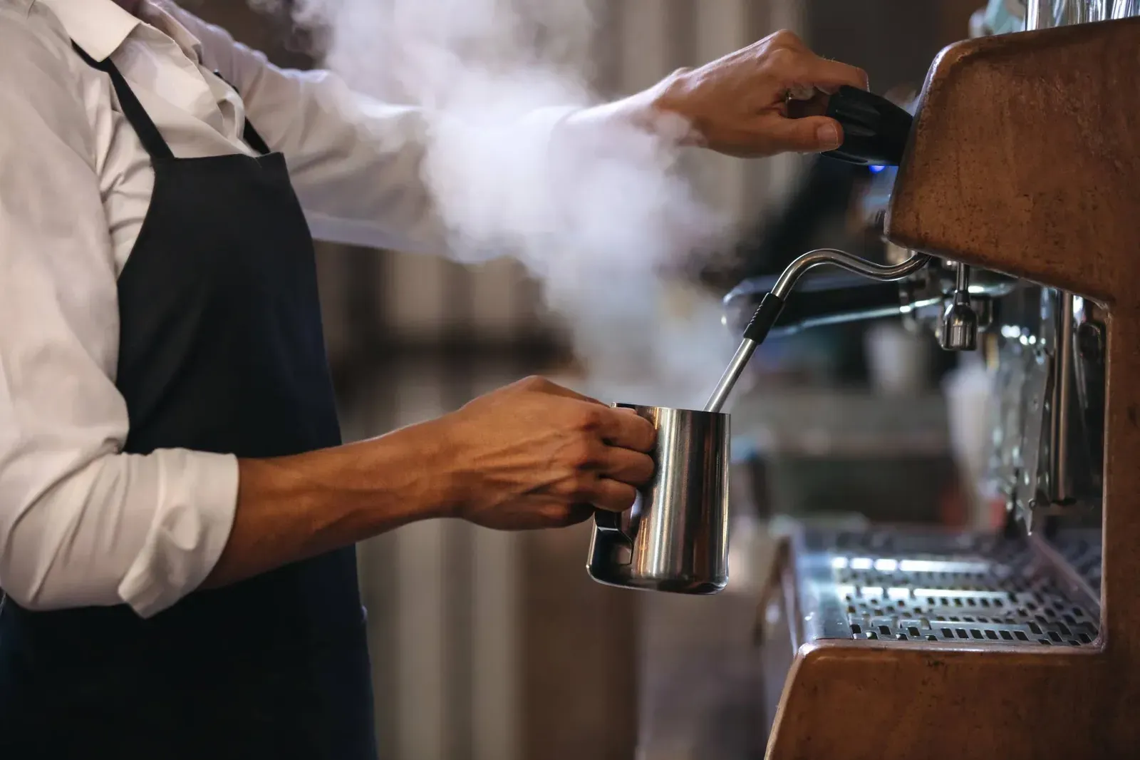 A barista steams milk in a stainless steel pitcher